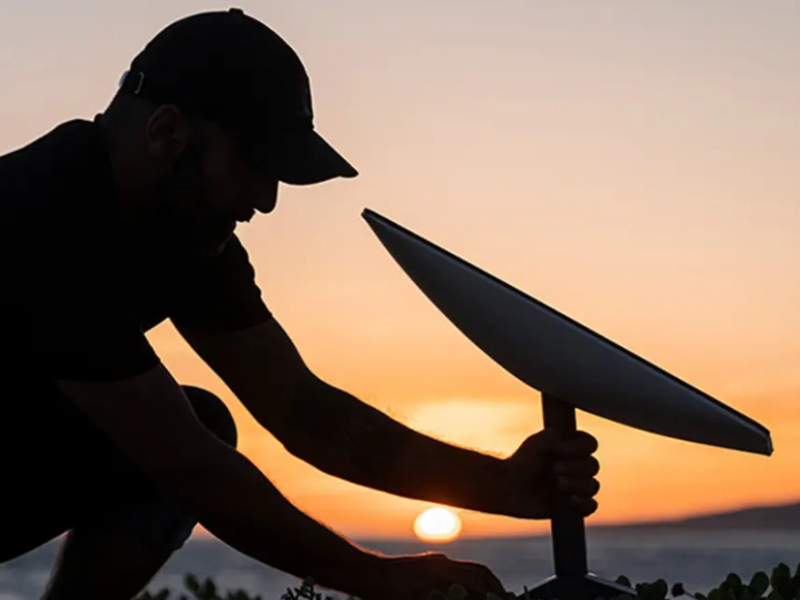 A NM Starlink installer setting up satellite dish on a customer's roof with a sunset backdrop in New Mexico.